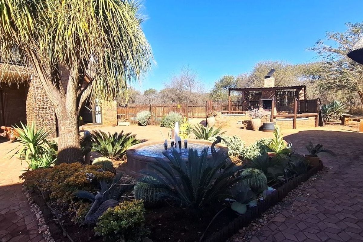 Spacious rear courtyard featuring stone-clad architecture, a central water fountain, brick paving, and a built-in outdoor braai area.