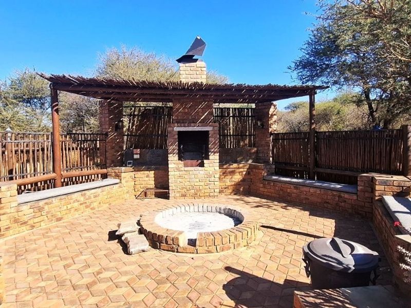 Outdoor entertainment area featuring a built-in brick braai, central fire pit, and integrated brick bench seating under a rustic thatched pergola.