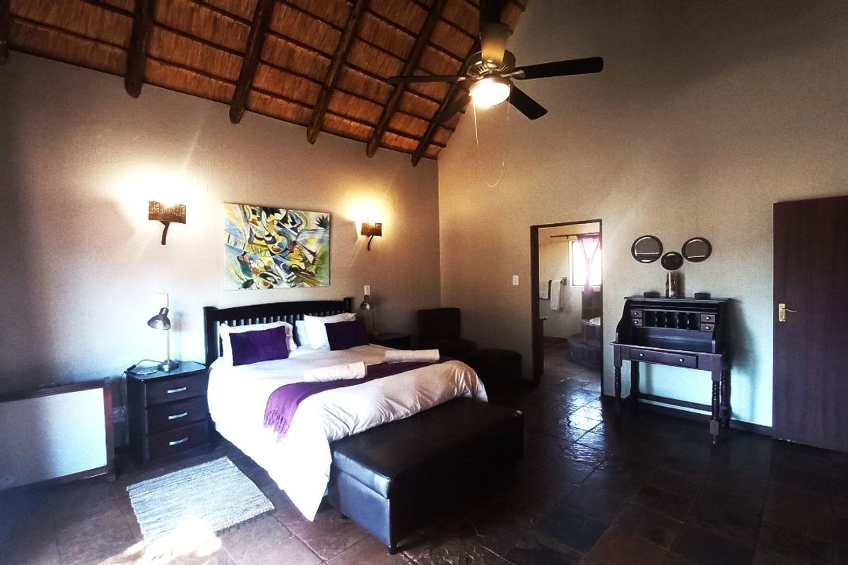 Spacious bedroom featuring a high vaulted thatched ceiling with exposed timber rafters, stone tile flooring, and integrated wall lighting.