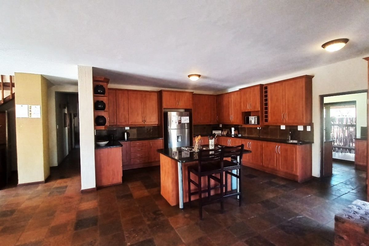 Spacious kitchen featuring warm-toned wooden cabinetry, granite countertops, a central island with a hob, and durable tiled flooring.