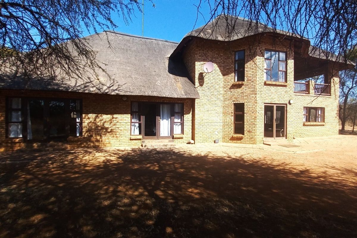 A rear view of a double-story face brick house featuring a traditional thatch roof, balcony, and multiple access points via sliding doors.