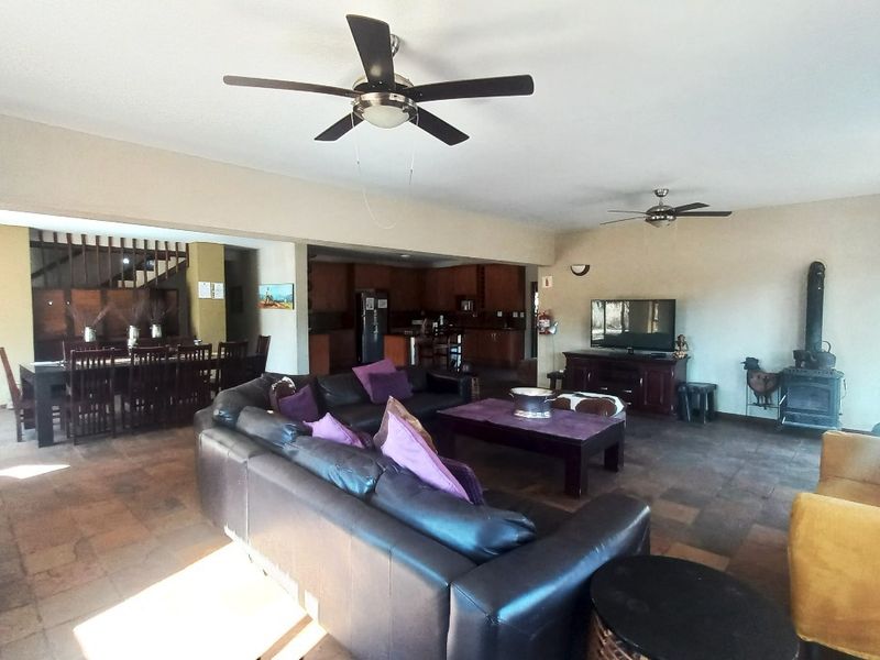 Spacious open-plan living and dining area featuring tiled floors, ceiling fans, and a cozy wood-burning fireplace, seamlessly connected to the kitchen.
