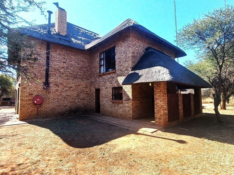 Rear view of a two-story face brick house featuring a traditional thatch roof, a covered patio area, and an external fire safety installation.