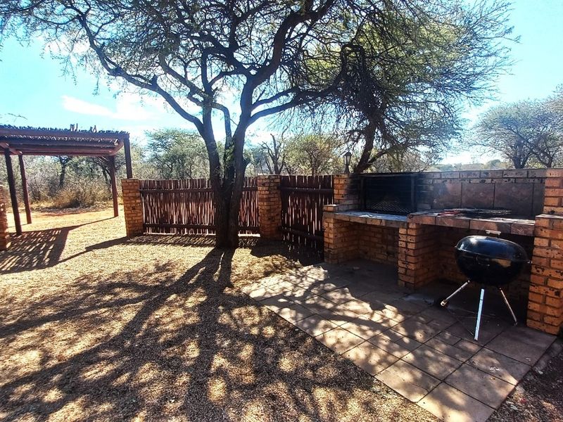 Outdoor entertainment area featuring a built-in brick braai, paved patio space, and a timber pergola set within a natural garden environment.