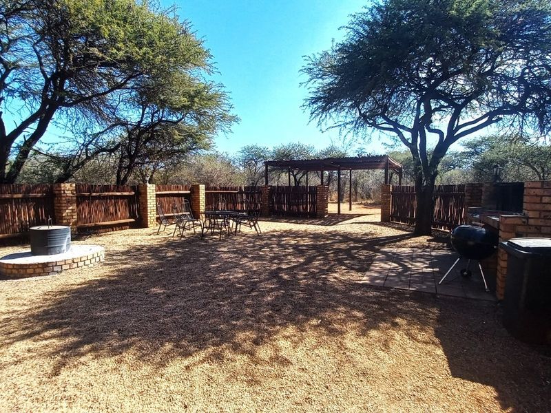 Outdoor entertainment area featuring a built-in brick braai, a raised circular fire pit, and a pergola, enclosed by brick and timber fencing.