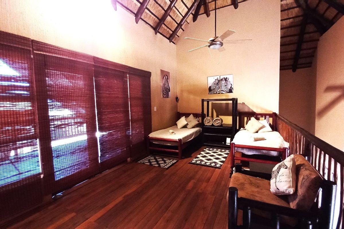 Spacious bedroom featuring a high vaulted thatched ceiling with exposed timber rafters, warm timber flooring, and a protective timber balustrade overlooking the lower level.