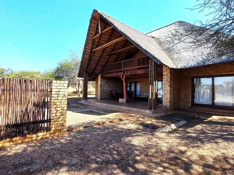 Rear view of a rustic brick house featuring a thatched roof, covered patio with timber supports, and a private fenced garden area.