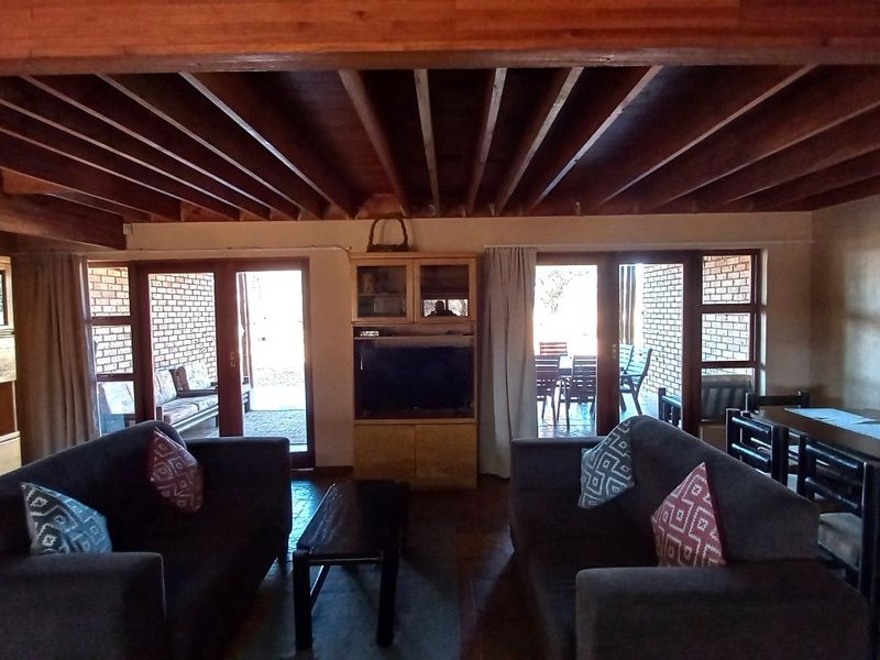 Spacious open-plan living and dining area featuring exposed timber beam ceilings, brick walls, and large sliding glass doors providing access to the patio.