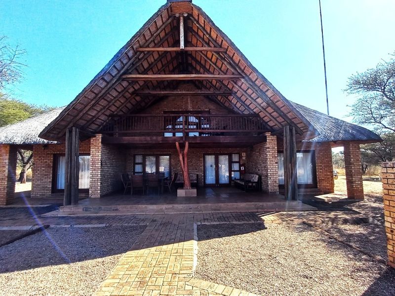 A charming thatched-roof house featuring a prominent timber-framed facade, a spacious covered patio, and a rustic brick exterior set in a natural landscape.