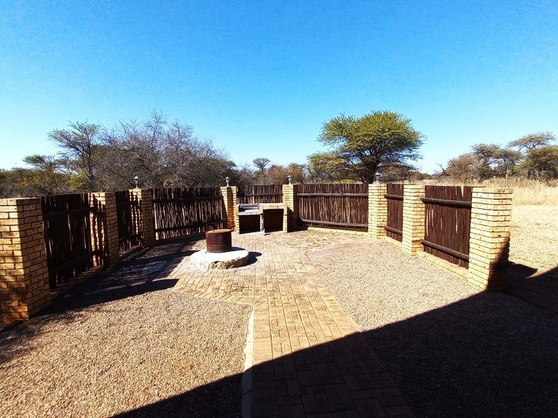 Outdoor entertainment area featuring a brick-paved patio, built-in braai, fire pit, and enclosed by a brick and timber fence in a natural bushveld setting.