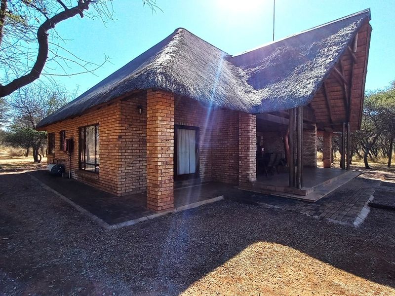 A charming face brick house featuring a traditional thatched roof and a spacious covered patio area, set within a natural bushveld environment.