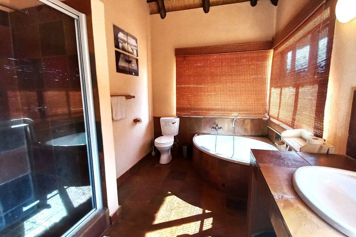 A rustic-style bathroom featuring a shower enclosure, oval bathtub, toilet, and vanity basin with warm-toned tiling and exposed timber ceiling beams.