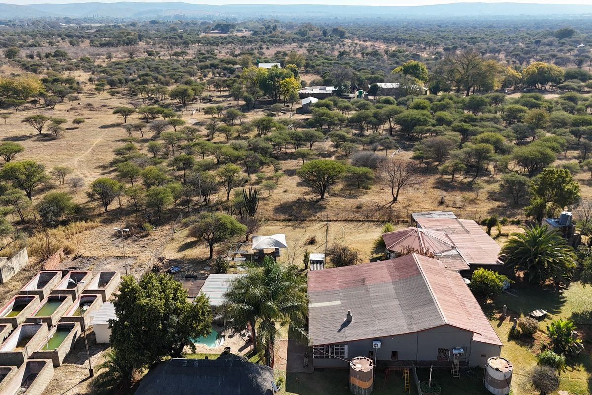 Aerial view of a small holding property featuring multiple outbuildings, water storage tanks, a swimming pool, and extensive surrounding bushveld landscape.
