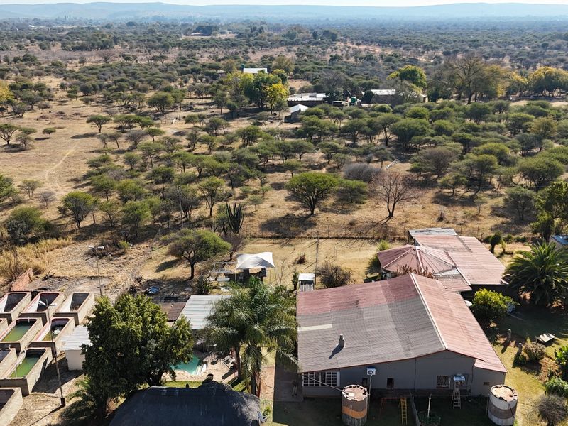 Aerial view of a small holding property featuring multiple outbuildings, water storage tanks, a swimming pool, and extensive surrounding bushveld landscape.