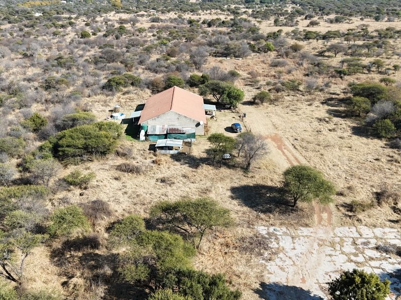Aerial view of a small holding property featuring a main structure with a pitched roof, set within a large, dry, open landscape.