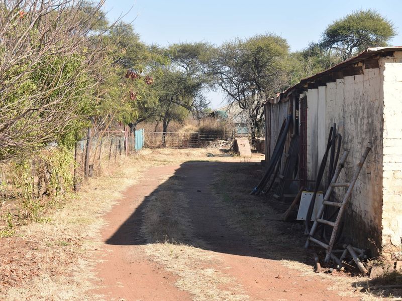 A view of a dirt path running alongside a weathered masonry and corrugated metal outbuilding on a small holding property.