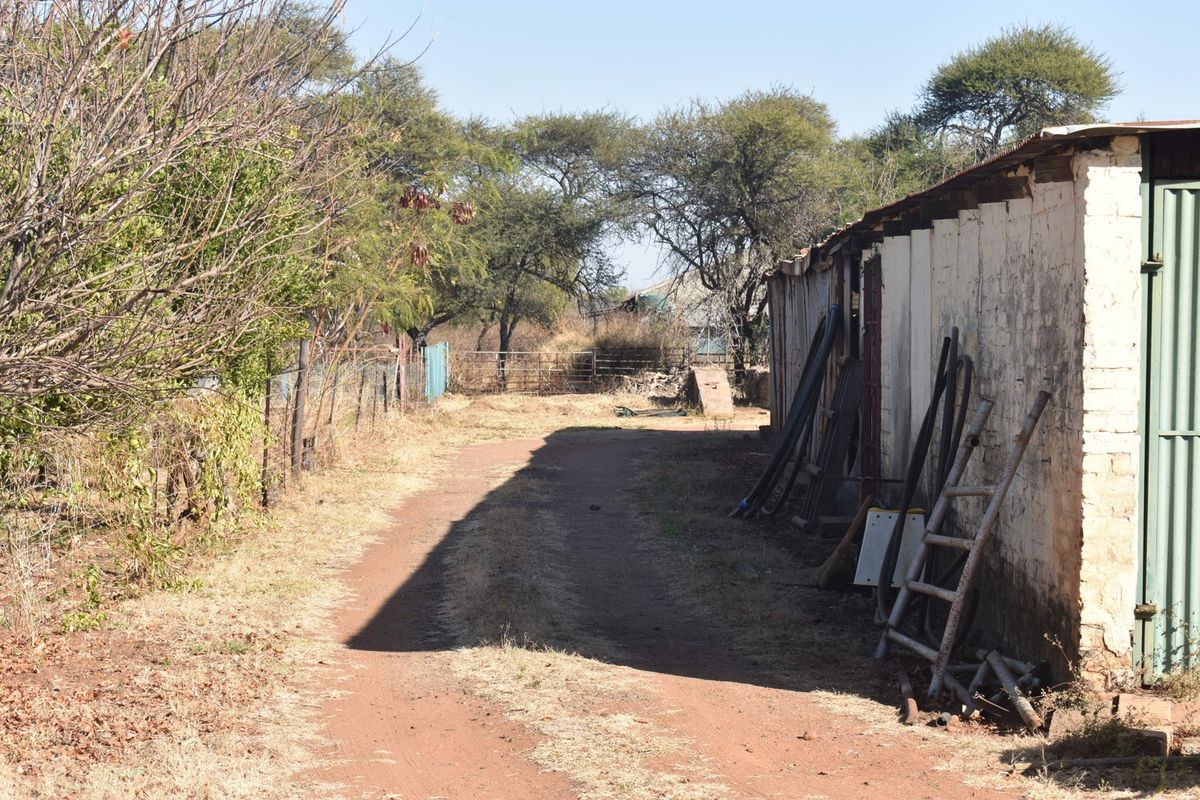 A view of a dirt path running alongside a weathered masonry and corrugated metal outbuilding on a small holding property.