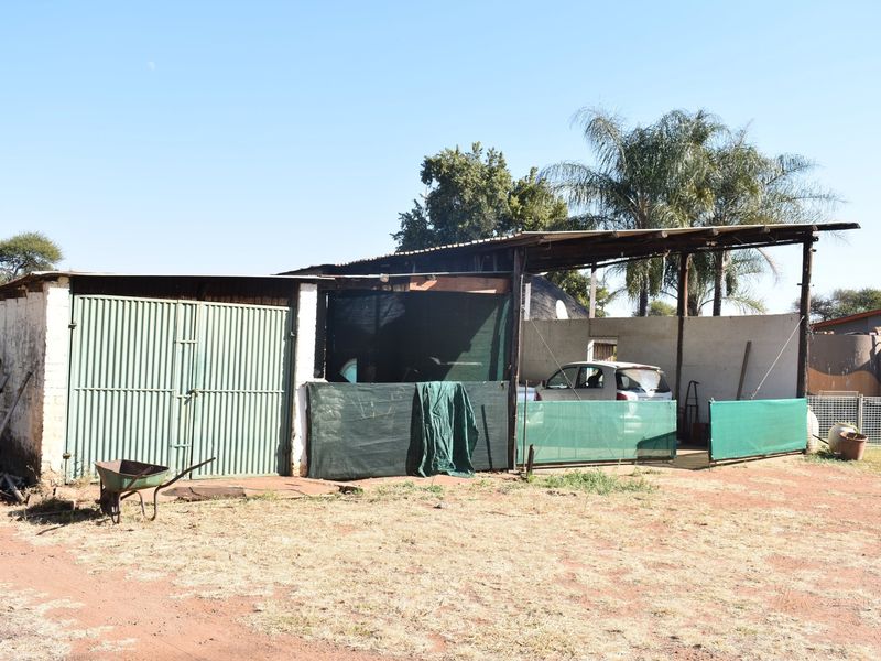 A functional outbuilding featuring a secure garage section and an adjacent open-sided carport structure with shade cloth screening.