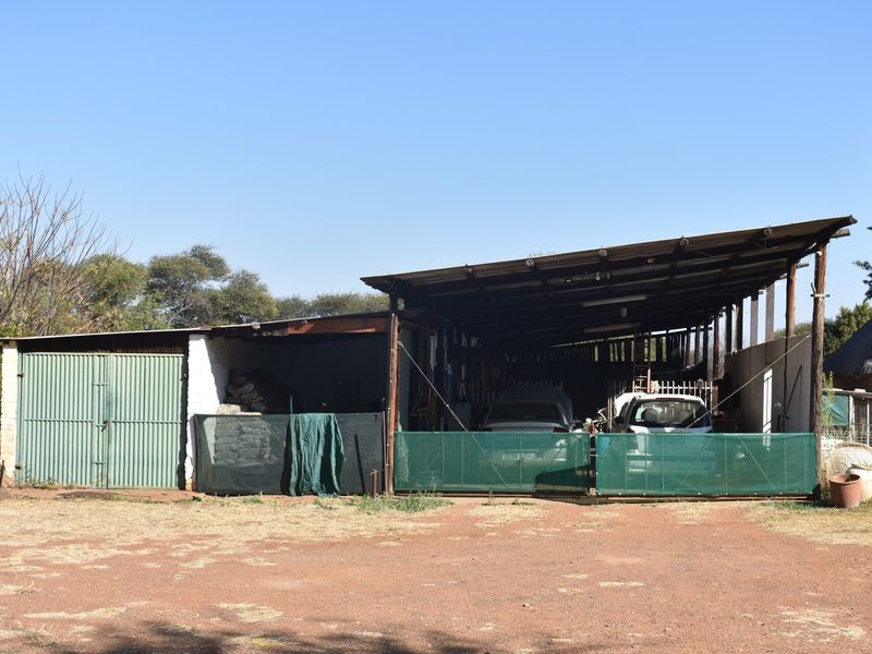 A large, open-sided corrugated metal garage structure providing covered parking and storage space on the small holding.