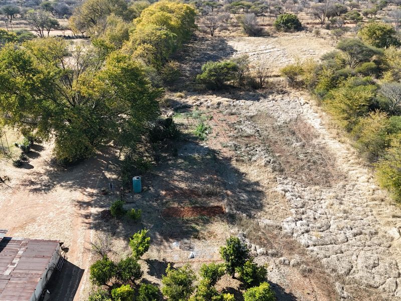 An aerial view of the small holding property showing the surrounding landscape, natural vegetation, and a portion of the main building's corrugated metal roof.