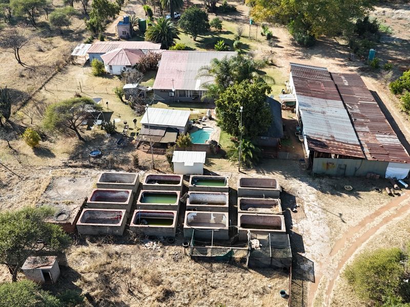 Aerial view of a small holding property featuring multiple outbuildings, a swimming pool, and several concrete water tanks on a large rural plot.