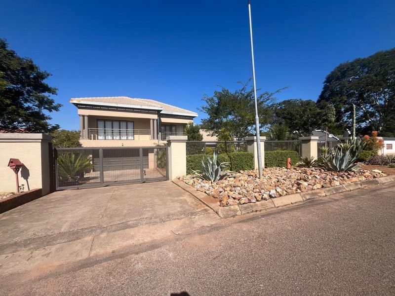 Front view of a two-story residential property featuring a concrete driveway, metal security gate, perimeter wall, and a balcony with metal railings.