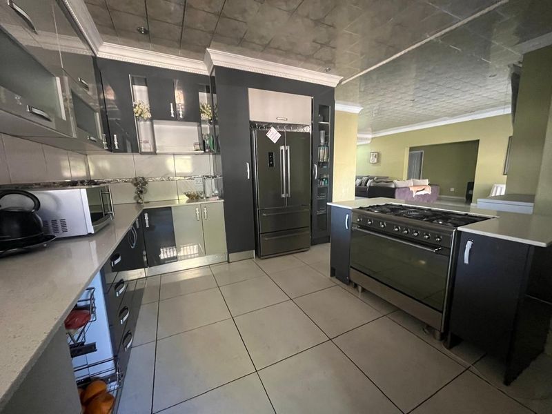 Modern kitchen featuring dark cabinetry, stone countertops, a large gas stove with oven, and tiled flooring, flowing into an adjacent living area.