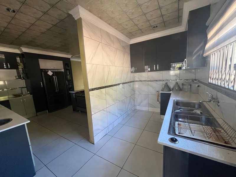 Modern kitchen featuring dark cabinetry, marble-look tiled walls, double sink, and tiled flooring with a distinct partition wall separating the cooking area.