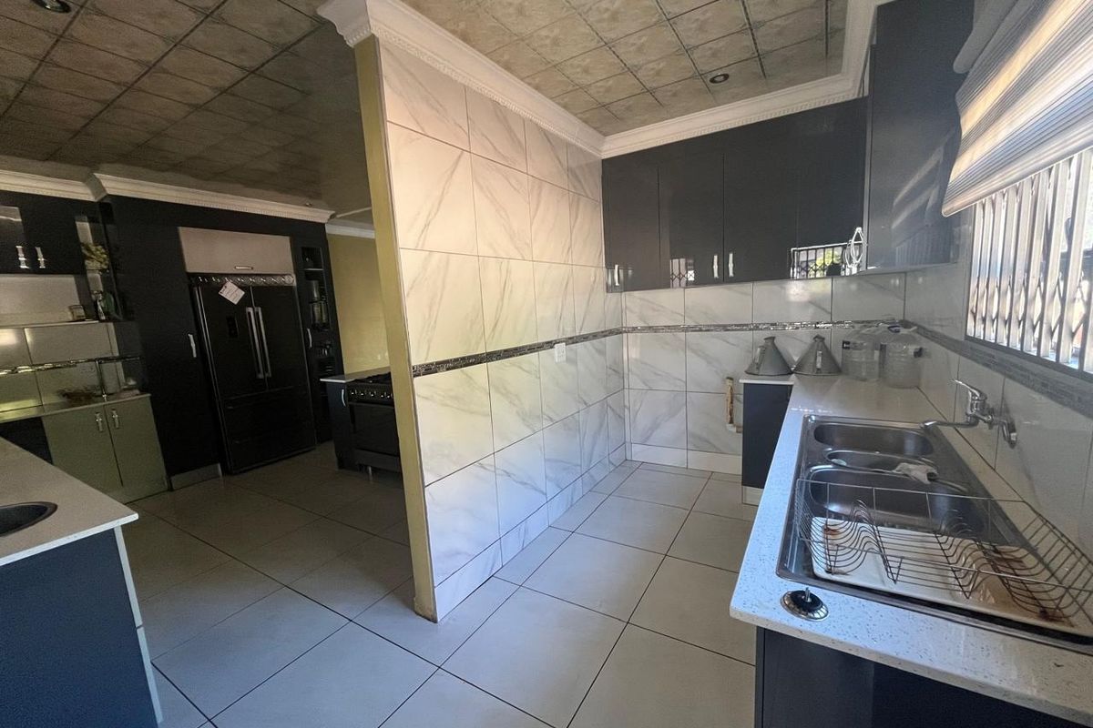 Modern kitchen featuring dark cabinetry, marble-look tiled walls, double sink, and tiled flooring with a distinct partition wall separating the cooking area.