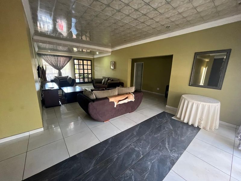 Spacious living area featuring large format floor tiles, a unique panelled ceiling, and direct access to outdoor space through a sliding glass door.