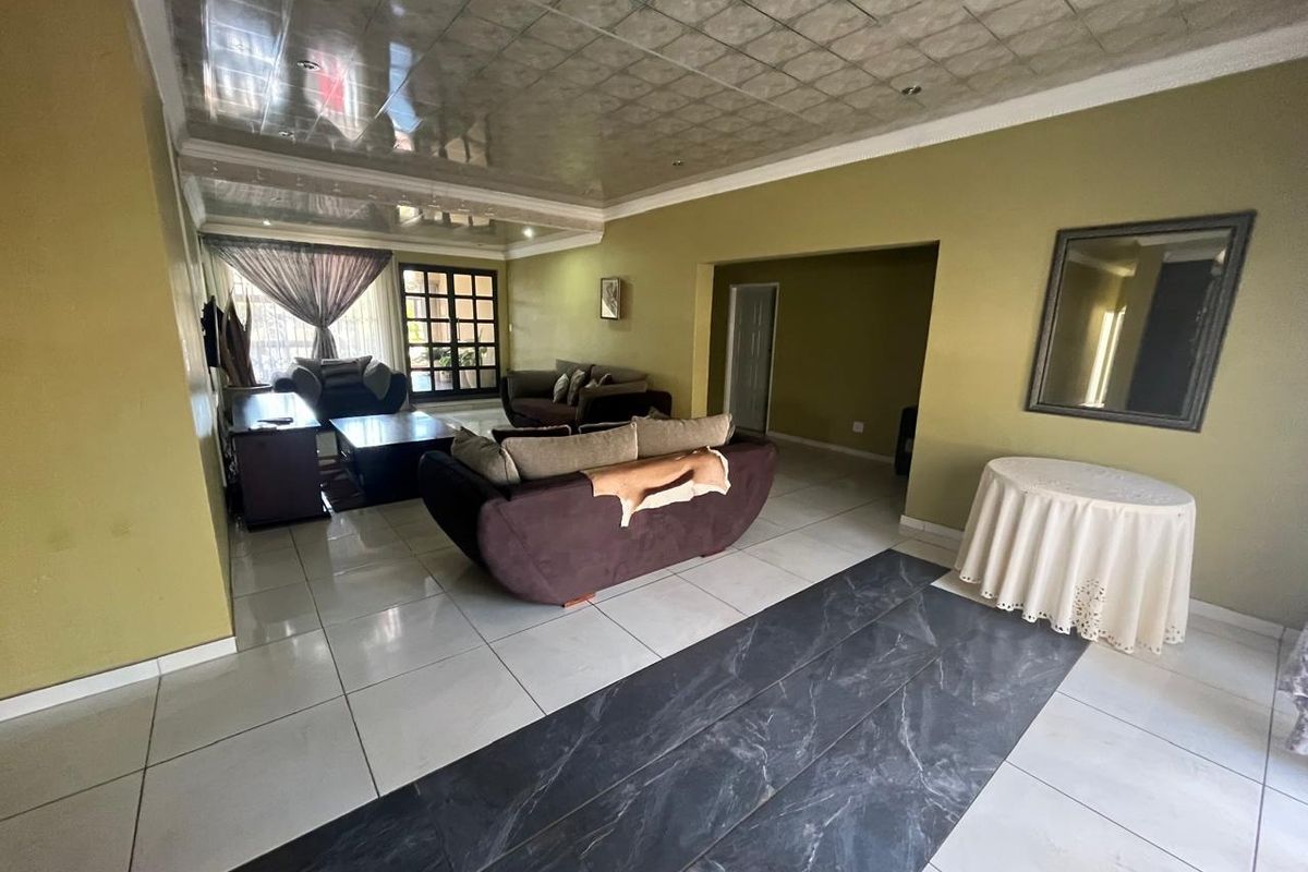 Spacious living area featuring large format floor tiles, a unique panelled ceiling, and direct access to outdoor space through a sliding glass door.