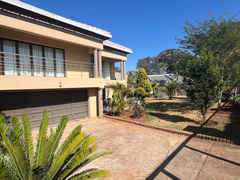 Front view of a double-story house featuring a double garage, a spacious balcony with stainless steel balustrades, and a paved driveway.