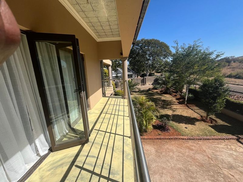 A spacious covered balcony featuring a metal balustrade and direct access to the garden area through double glass doors.