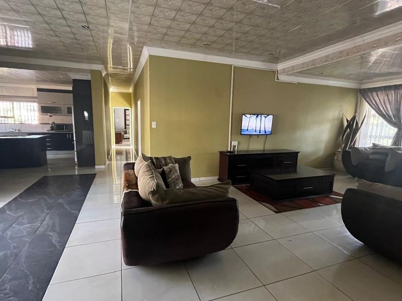 Spacious open-plan living area featuring tiled floors, recessed ceiling panels, and a connected kitchen with modern cabinetry and a central island.