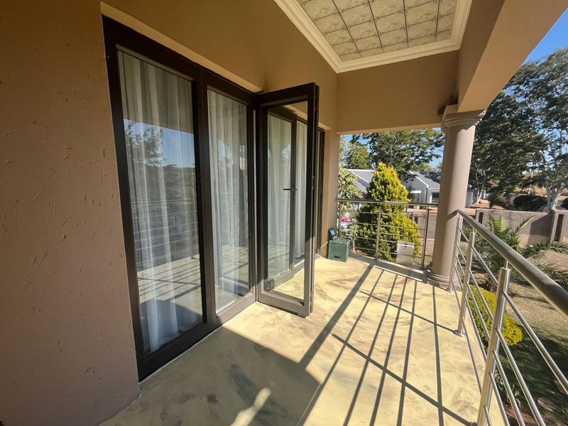 A covered balcony featuring a stainless steel balustrade, tiled ceiling detail, and aluminium framed glass doors leading into the home.