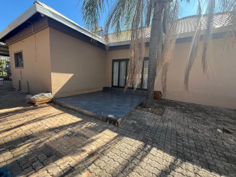 Rear exterior view featuring a tiled patio area, paved ground, and sliding glass door access to the main house structure.