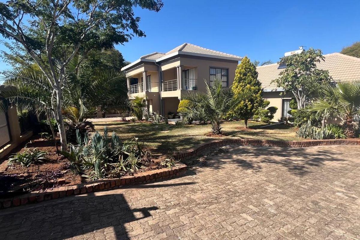 A spacious rear exterior view of a two-story house featuring a paved driveway, landscaped garden, and an upper-level balcony.