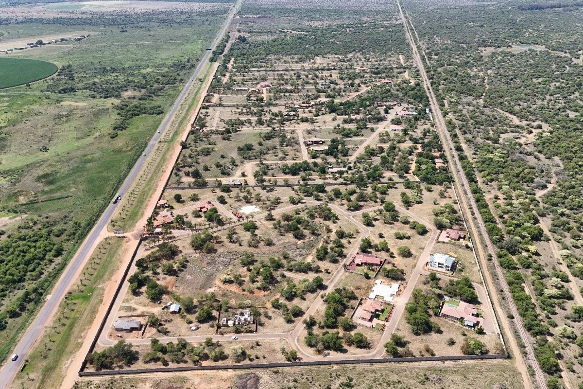 An aerial view of a residential estate featuring established plots, internal road networks, and perimeter fencing within a natural landscape setting.