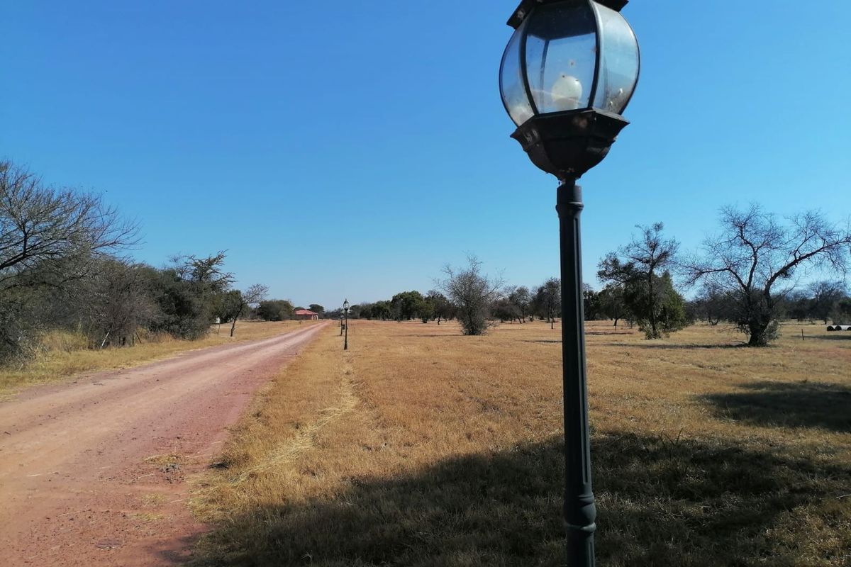 A view of a dirt road leading through a vacant residential plot, featuring installed street lighting along the path.