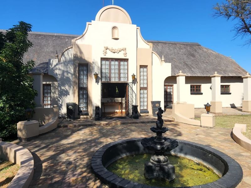 A distinctive Cape Dutch style home featuring a thatched roof, decorative gable, and a central stone-paved courtyard with a water fountain.