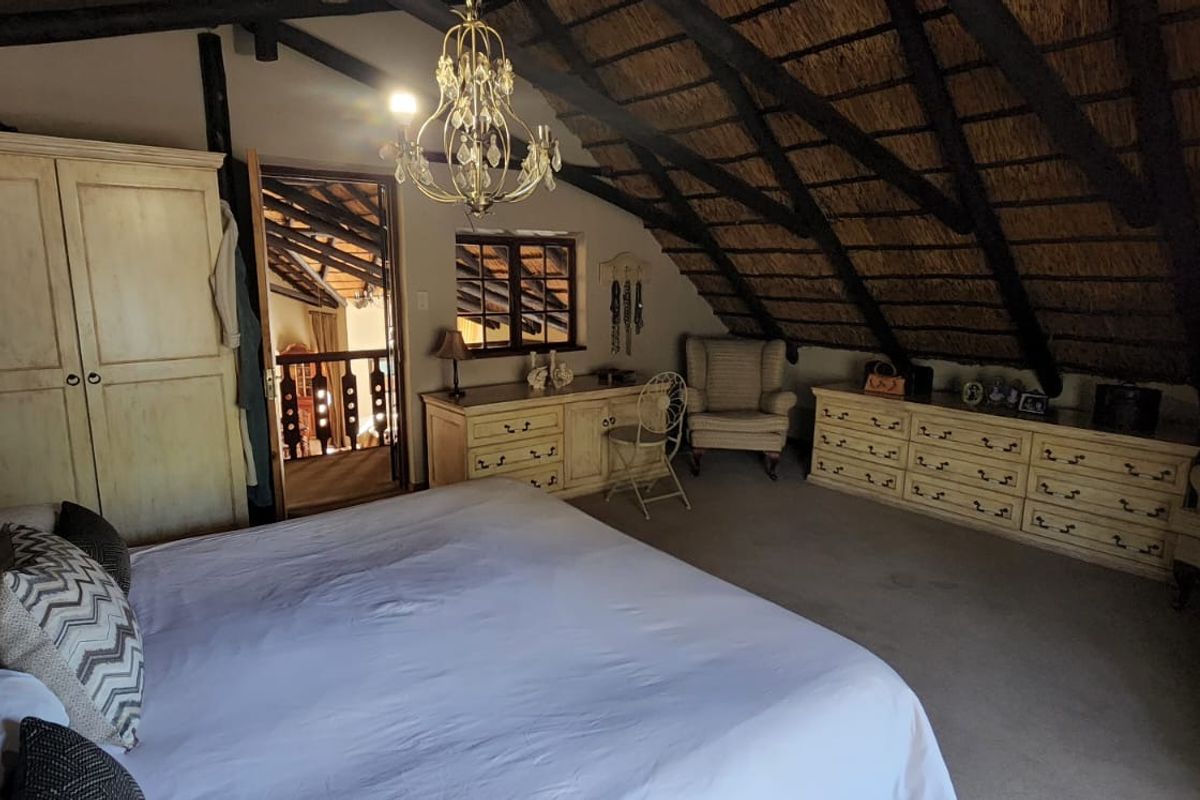 Spacious bedroom featuring a unique vaulted thatched roof with exposed timber rafters and a classic chandelier, creating a rustic and cozy atmosphere.