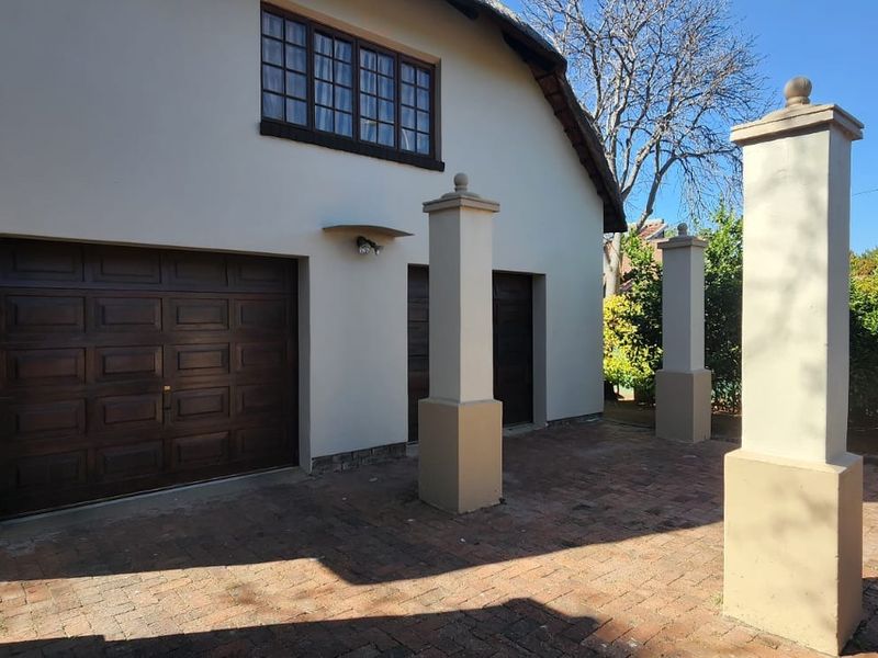 Exterior view of a double garage featuring dark timber doors, brick paving, and decorative masonry pillars under a traditional thatched roof.
