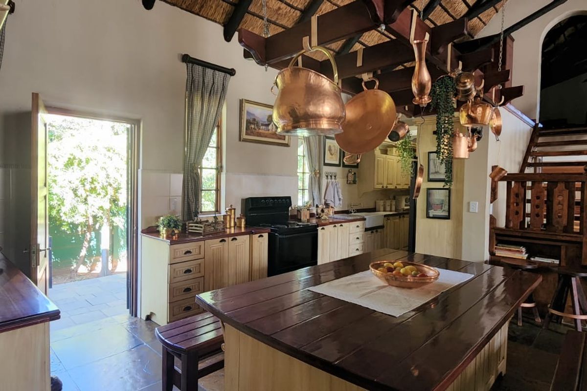 Rustic kitchen featuring timber cabinetry, a central island, exposed timber beams, and a thatched ceiling, with direct access to an outdoor patio area.