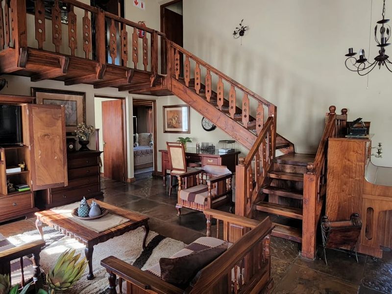 Spacious living area featuring a prominent wooden staircase leading to a mezzanine level, stone flooring, and a high thatched ceiling.