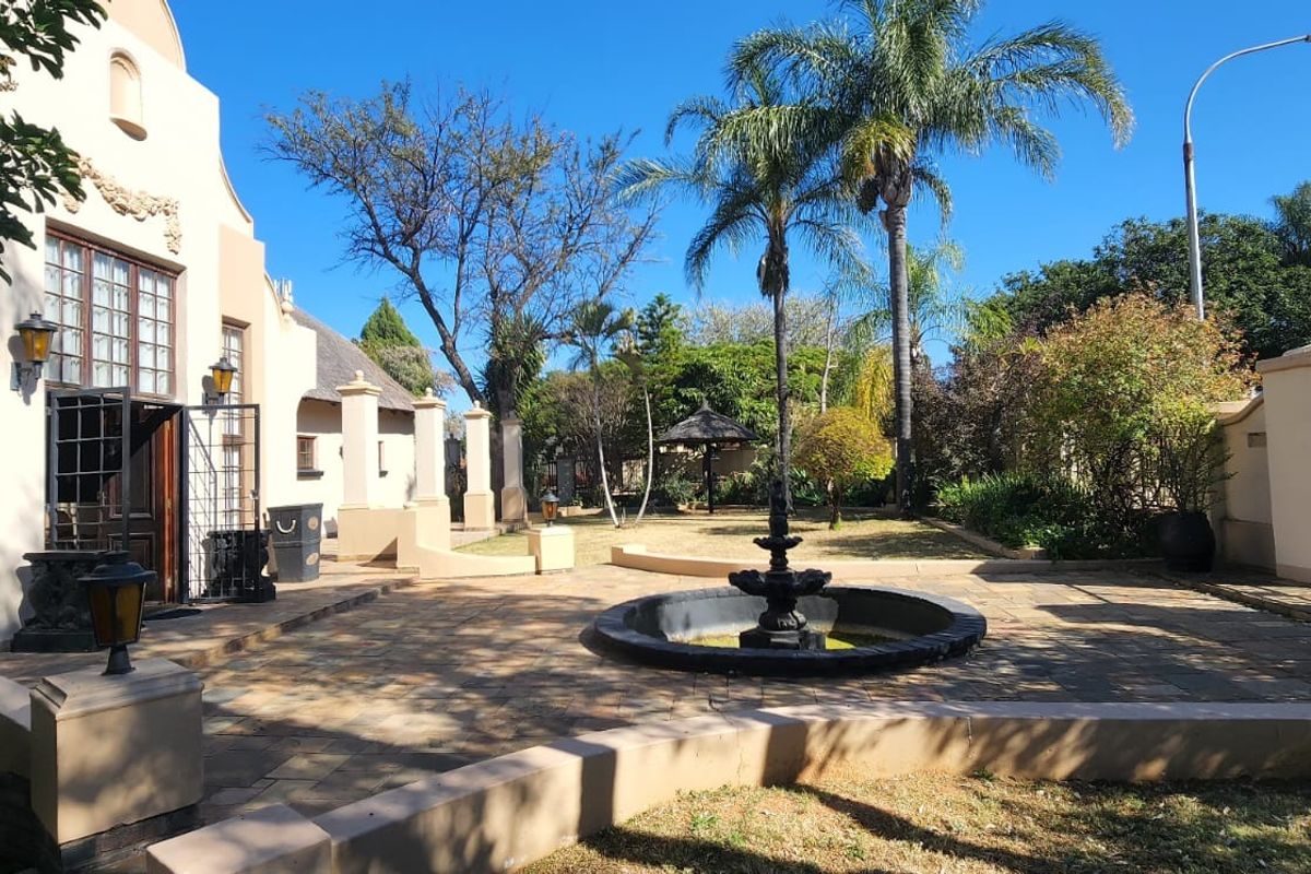 Spacious rear courtyard featuring stone paving, a central decorative water fountain, and established garden surroundings with a thatched gazebo.