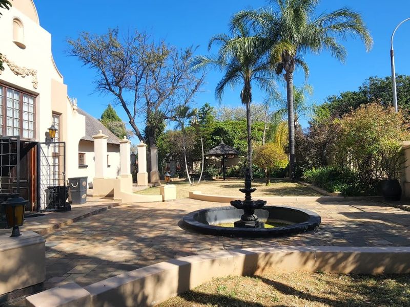 Spacious rear courtyard featuring stone paving, a central decorative water fountain, and established garden surroundings with a thatched gazebo.