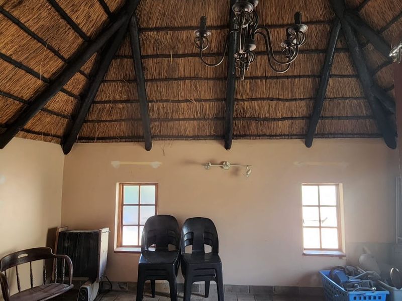 Living area featuring a high vaulted thatched roof with exposed timber beams, wrought iron chandelier, and timber frame windows.