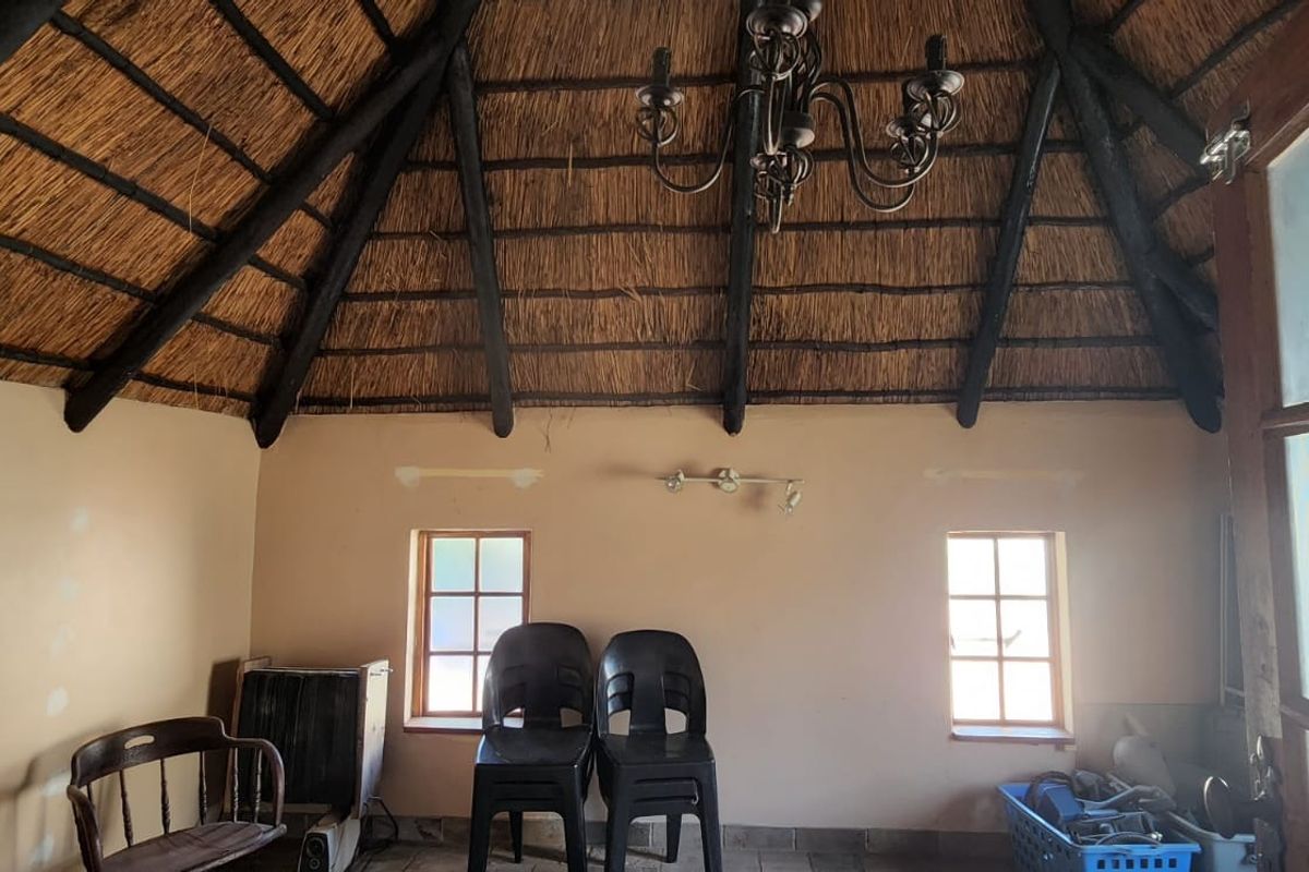 Living area featuring a high vaulted thatched roof with exposed timber beams, wrought iron chandelier, and timber frame windows.