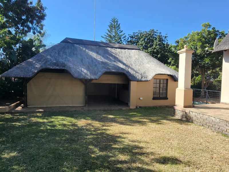 Rear view of the property featuring a thatched-roof outdoor entertainment area, paved patio, and established garden space.