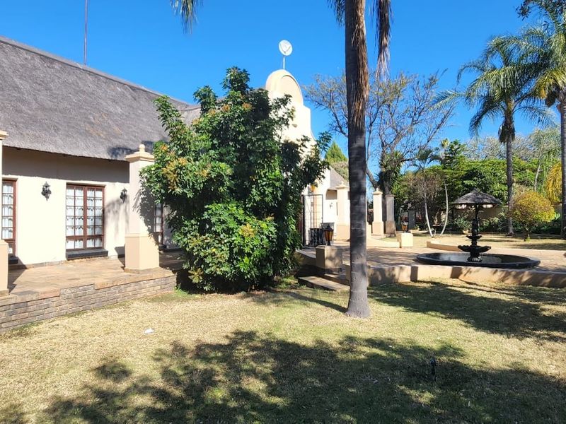 Rear view of a house with a thatched roof, featuring a paved patio area, masonry pillars, and a decorative garden fountain.